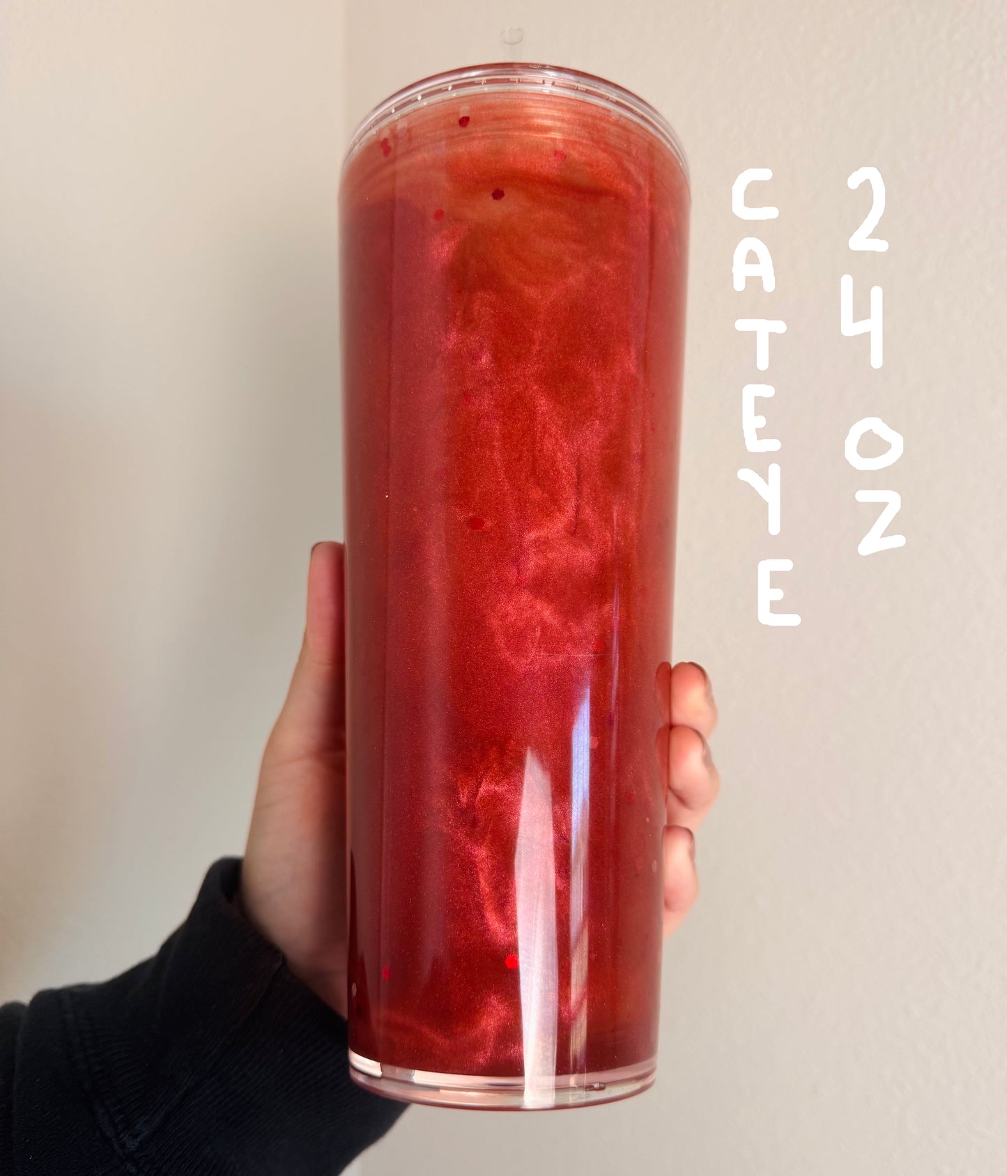 Hand holding a tall cylindrical container with a red marbled pattern against a plain background